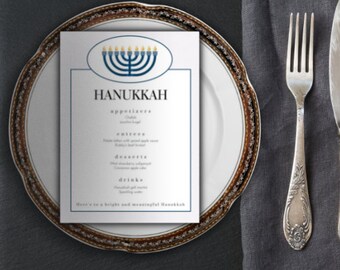 May include: A white card with a blue and gold menorah design and the word "Hanukkah" printed in black. The card lists a menu for a Hanukkah dinner with appetizers, entrees, desserts, and drinks. The card is on a white plate with a gold rim.