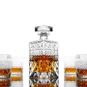 May include: A crystal decanter with a square base and a stopper, filled with amber liquid, surrounded by four crystal glasses, also filled with amber liquid. The glasses and decanter have a diamond-shaped pattern.
