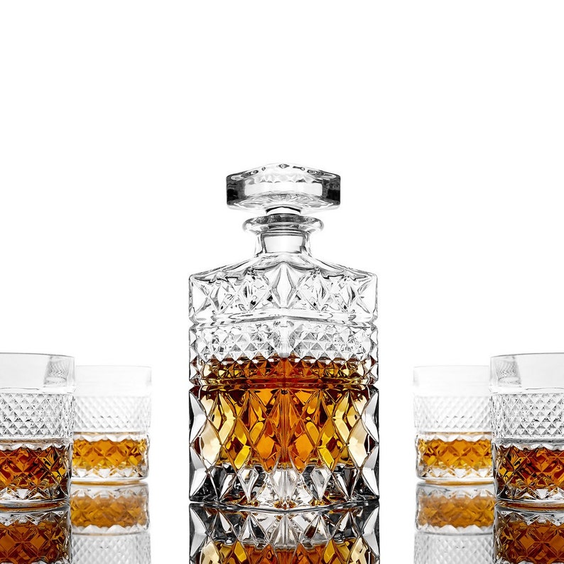 May include: A crystal decanter with a square base and a stopper, filled with amber liquid, surrounded by four crystal glasses, also filled with amber liquid. The glasses and decanter have a diamond-shaped pattern.