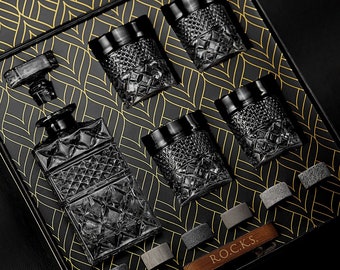 Może przedstawiać: Zestaw sześciu czarnych szklanek do whisky z geometrycznym wzorem. Szklanki są ułożone w czarnym pudełku z złotym wzorem. Pudełko zawiera również czarną szklaną karafkę z geometrycznym wzorem. Na pudełku widnieje napis "ROCKS".