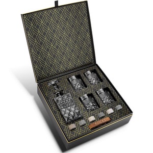 May include: A black gift box with a gold patterned lid is open to reveal a crystal decanter and six crystal glasses. The box also includes a set of whiskey stones and a leather tag that says "Rocks".
