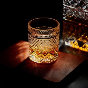 May include: A clear glass with a diamond pattern is filled with amber-colored liquid. The glass sits on a brown surface.