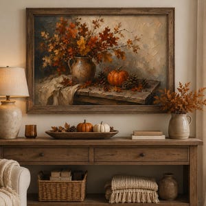 May include: A framed oil painting depicting a rustic autumn still life with a ceramic pitcher filled with orange and brown fall leaves, a small pumpkin, and pinecones on a wooden table, displayed above a wooden console table with seasonal decor.