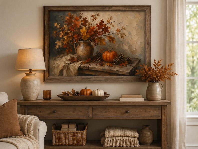 May include: A framed oil painting depicting a rustic autumn still life with a ceramic pitcher filled with orange and brown fall leaves, a small pumpkin, and pinecones on a wooden table, displayed above a wooden console table with seasonal decor.