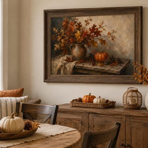 May include: A framed oil painting depicting a still life scene with a ceramic pitcher filled with autumn leaves, a pumpkin, and pinecones on a wooden table. The artwork features warm orange, brown, and cream tones, displayed in a dark wood frame.