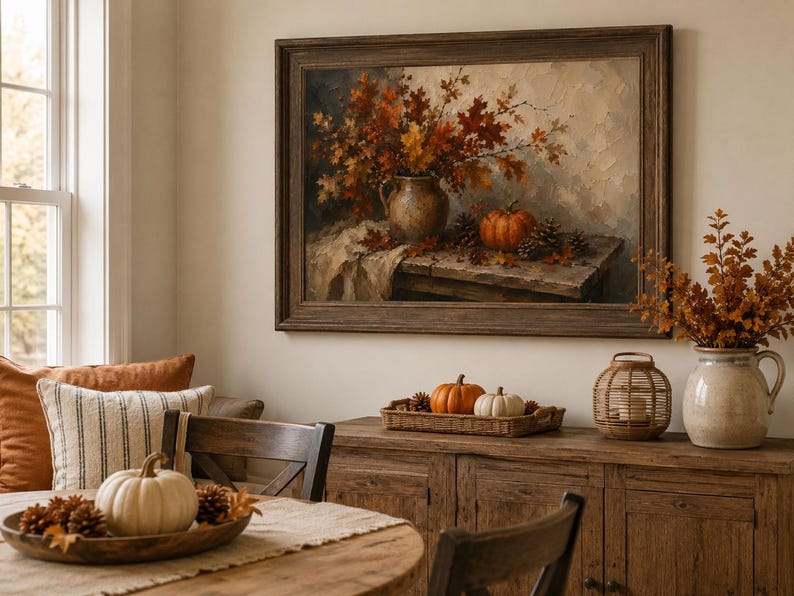 May include: A framed oil painting depicting a still life scene with a ceramic pitcher filled with autumn leaves, a pumpkin, and pinecones on a wooden table. The artwork features warm orange, brown, and cream tones, displayed in a dark wood frame.