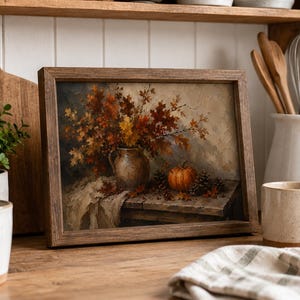 May include: A framed rectangular wall art print featuring an oil painting of a rustic ceramic pitcher filled with autumn leaves, a small orange pumpkin, and pinecones resting on a wooden table surface with a draped fabric cloth underneath.