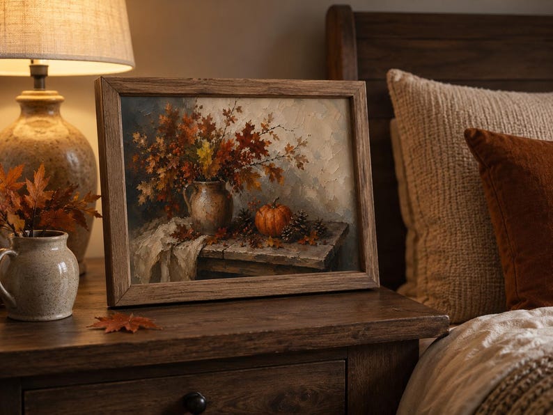 May include: A framed oil painting depicting a still life scene with a ceramic pitcher filled with autumn leaves, a small orange pumpkin, and pinecones resting on a wooden table, rendered in warm shades of brown, orange, and cream.