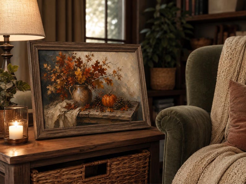 May include: A framed oil painting depicting a rustic autumn still life scene. The artwork features a ceramic pitcher filled with vibrant orange and brown maple leaves, a small orange pumpkin, and scattered pinecones on a wooden table surface.