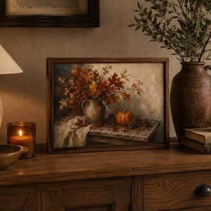 May include: A rectangular framed oil painting depicting a still life scene with a ceramic pitcher filled with autumn leaves, a small orange pumpkin, and pinecones resting on a wooden table draped with a piece of white fabric.