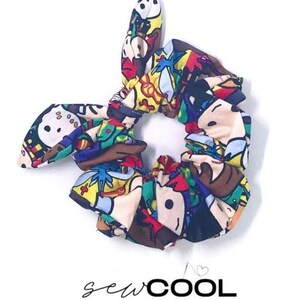 May include: A colorful hair scrunchie with a cartoon character print. The scrunchie is made of fabric and has a knotted design. The scrunchie is tied in a bow. The text "sewCOOL BY RUBY" is printed below the scrunchie.