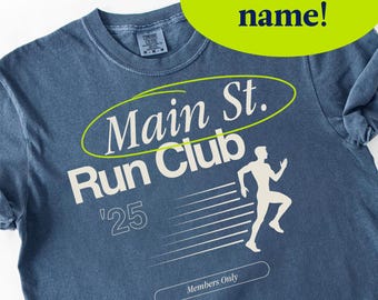 May include: A blue t-shirt with the text "Main St. Run Club" and a running figure graphic. The shirt also features the text "'25" and "Members Only". A green oval with the text "Custom name!" is at the top.