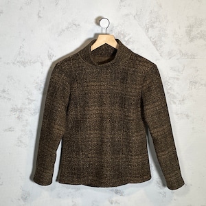 Peut inclure: Un pull à col roulé marron avec un motif texturé. Le pull est suspendu à un cintre en bois sur un fond blanc.