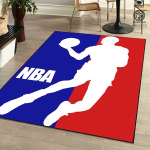May include: A blue and red rug with the NBA logo and a silhouette of a basketball player. The logo says "NBA" in white letters.