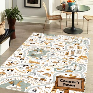 May include: A white and beige play mat with a winding road design. The mat features various illustrations of animals, vehicles, and buildings. The text "Cooper's Town" is displayed on a wooden sign.