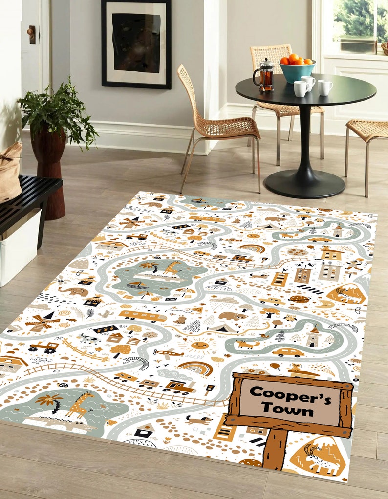 May include: A white and beige play mat with a winding road design. The mat features various illustrations of animals, vehicles, and buildings. The text "Cooper's Town" is displayed on a wooden sign.