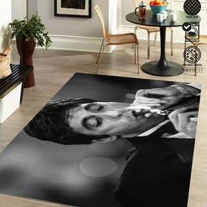 May include: Black and white rug featuring a close-up of a man's face. The man is smoking a cigarette and has a serious expression. The rug is made of a soft, durable material and is perfect for adding a touch of style to any room.