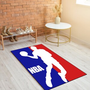 May include: A blue and red NBA logo rug with a white silhouette of a basketball player dribbling a ball. The rug has the word "NBA" in white letters.