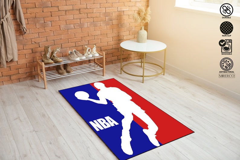 May include: A blue and red NBA logo rug with a white silhouette of a basketball player dribbling a ball. The rug has the word "NBA" in white letters.