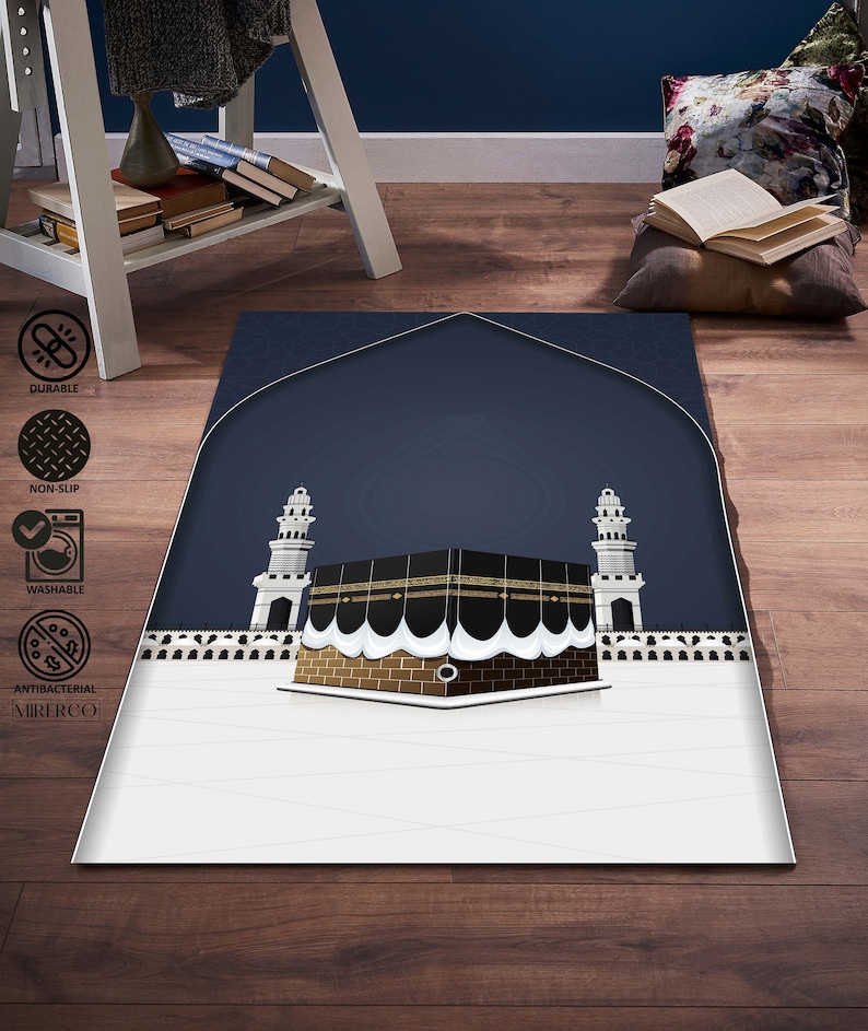 May include: A white and blue prayer rug with a depiction of the Kaaba, a cube-shaped building in Mecca, Saudi Arabia. The rug has a dark blue background with a white border and a white design of the Kaaba in the center. The rug is made of a soft, durable material and is perfect for use in prayer.