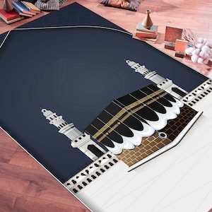 May include: A blue prayer rug with a white and gold design featuring the Kaaba, a cube-shaped building in Mecca, Saudi Arabia, and two minarets. The rug has a non-slip backing and is machine washable.