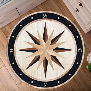 May include: A round rug with a compass design. The rug has a white background with a dark blue border and a brown and black compass rose in the center. The compass rose has the letters N, S, E, and W around the outside. The rug is perfect for adding a nautical touch to any room.