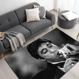 May include: Black and white rug featuring a close-up of a man's face with a cigarette in his mouth. The rug has a textured surface and is designed to be non-slip, durable, washable, and antibacterial.