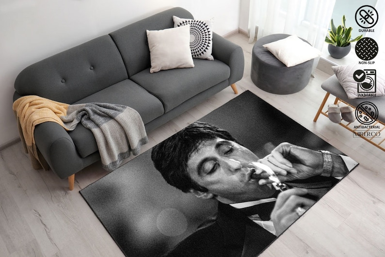May include: Black and white rug featuring a close-up of a man's face with a cigarette in his mouth. The rug has a textured surface and is designed to be non-slip, durable, washable, and antibacterial.