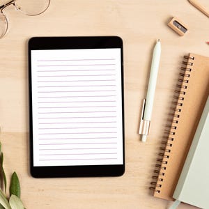 Tablet displaying a lined stationery page with purple rule lines, styled with a stylus, spiral notebooks, and glasses on a wooden desk.