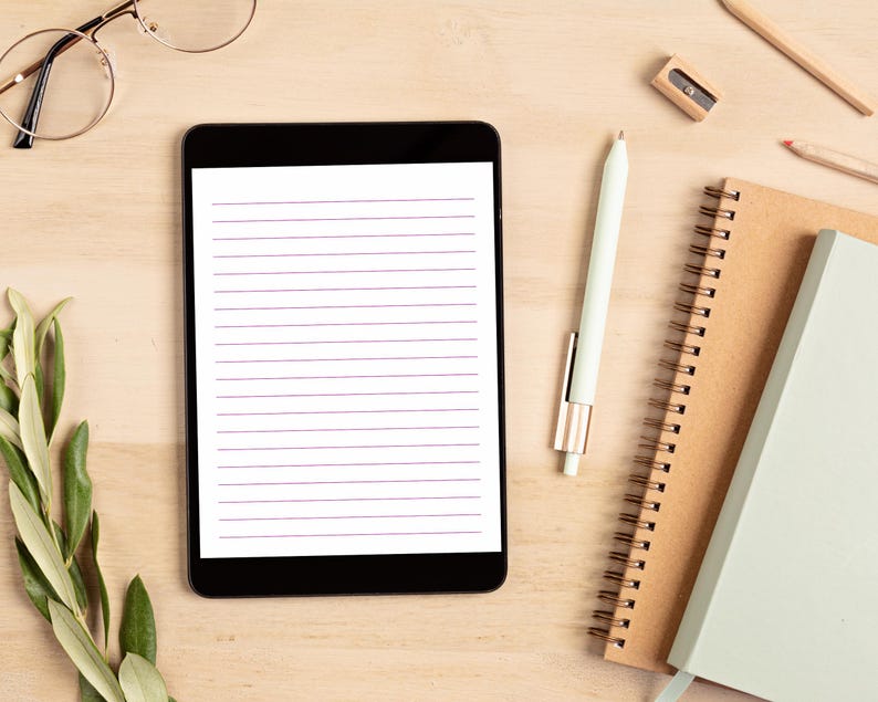 Tablet displaying a lined stationery page with purple rule lines, styled with a stylus, spiral notebooks, and glasses on a wooden desk.