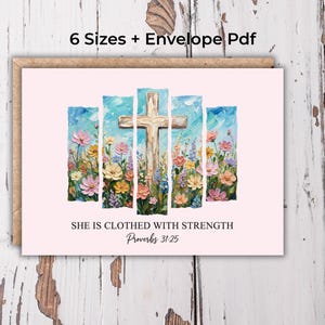 Op de afbeelding: Een wenskaart met een lichtroze achtergrond toont een houten kruis en kleurrijke bloemen. De tekst "SHE IS CLOTHED WITH STRENGTH Proverbs 31:25" staat eronder. De kaart is omlijst door een bruine rand.