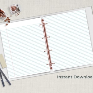 Blue lined notebook paper in an open three ring binder with pencils and copper paper clips on a neutral desk surface.