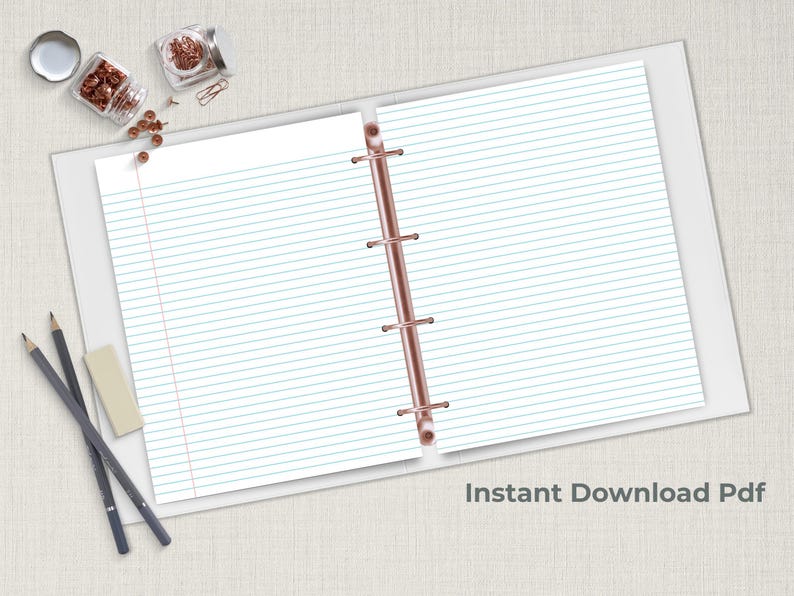 Blue lined notebook paper in an open three ring binder with pencils and copper paper clips on a neutral desk surface.
