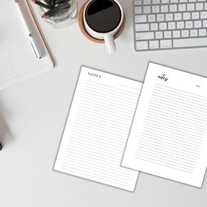 Two blank lined sheets of paper with the word "NOTES" at the top of each sheet. The sheets are on a white surface with a keyboard, a cup of coffee, and a notebook.