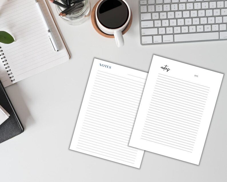 Two blank lined sheets of paper with the word "NOTES" at the top of each sheet. The sheets are on a white surface with a keyboard, a cup of coffee, and a notebook.