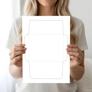 Envelope template sheet held by a woman in front of a bright white background, showing solid cut lines and dotted fold lines.
