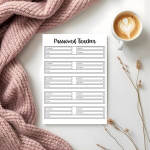 Password tracker page with labeled fields arranged on a white surface beside a soft pink knit blanket, a cup of coffee, and dried floral stems.