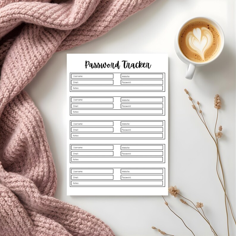 Password tracker page with labeled fields arranged on a white surface beside a soft pink knit blanket, a cup of coffee, and dried floral stems.