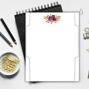 Envelope template with floral design in burgundy and orange fall colors, shown flat on a desk with stationery supplies.