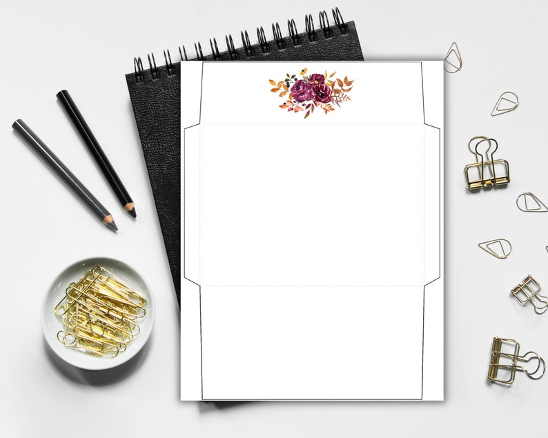 Envelope template with floral design in burgundy and orange fall colors, shown flat on a desk with stationery supplies.