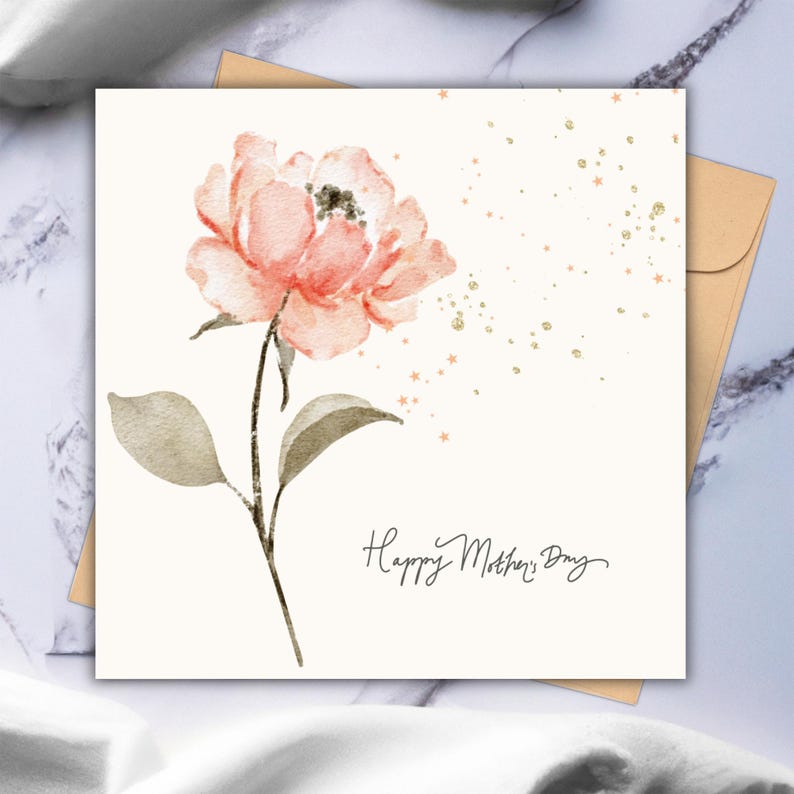 Square floral greeting card with a soft pink watercolor flower and gold accent details, displayed on a styled surface with a neutral envelope behind it.