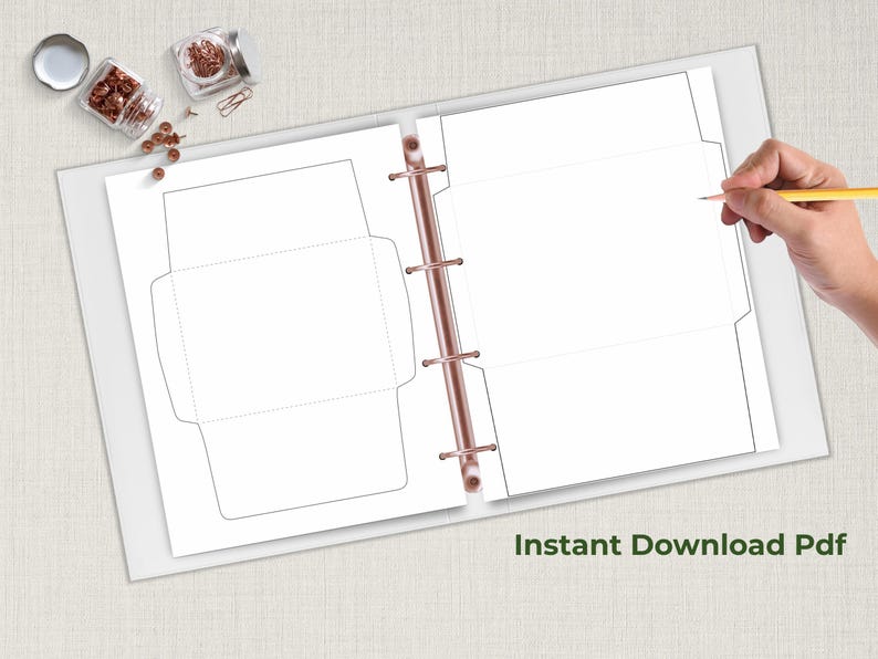 Open binder displaying two envelope template sheets with solid and dotted cut-and-fold lines, shown on a neutral desk beside stationery items.