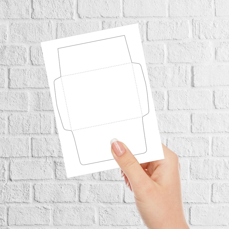 Envelope template held by a hand in front of a white brick background, showing solid cut lines and dotted fold lines on a plain sheet.