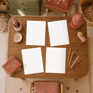 Four handwriting practice pages with red and blue lines on a wooden table with a pencil.