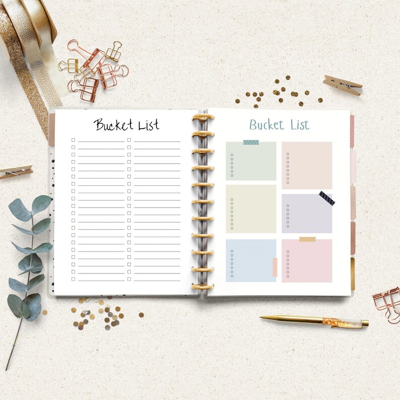 Open ring binder planner showing two bucket list pages with checklist lines and colorful note boxes surrounded by a pen, ribbon, paper clips, eucalyptus leaves, and gold confetti on a light surface.