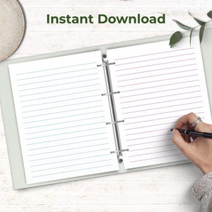 An open binder displays two sheets of lined note paper, with a hand writing on the right page on a light wooden desk.