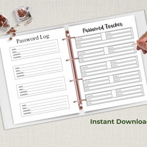 Open ring binder on a neutral fabric background showing two password organizer pages, one labeled Password Log and one labeled Password Tracker, with a hand writing on the page and small jars nearby.