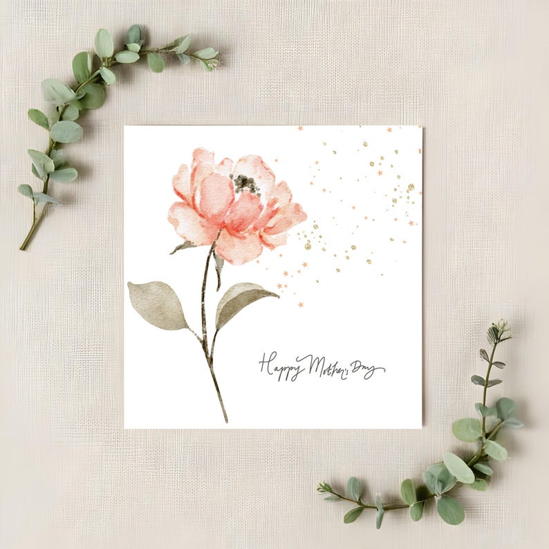 Square Mother’s Day card with watercolor blush flower and gold speckles styled on neutral linen background with greenery accents.