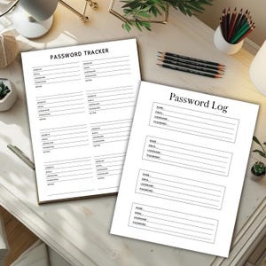 Two black and white password tracker pages displayed on a light wooden desk with plants, pencils, and desk accessories in a styled workspace setting.