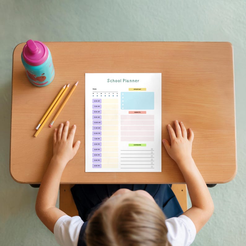 Top-down view of a child sitting at a small wooden desk with a single colorful page centered on the surface, featuring multiple colored sections arranged in columns, with pencils and a drink bottle nearby.